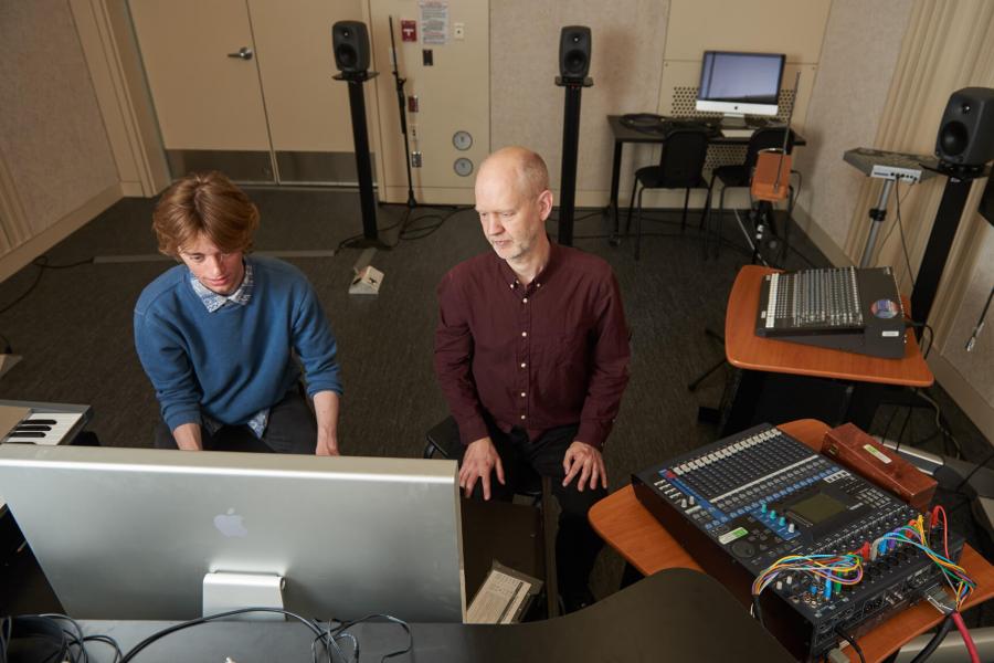 Two people seated at a desk inside the electro-acoustic composition lab surrounded by various equipment. 