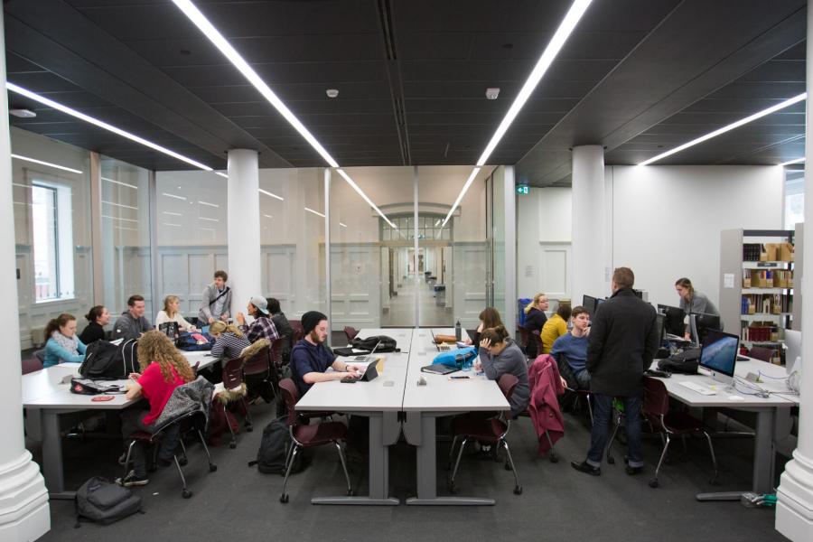 Students study and work at rows of tables in the seating area of the music library. 