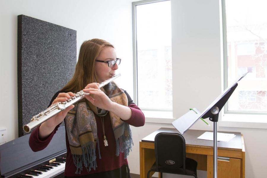 A music student practices the flute in a practice room. 