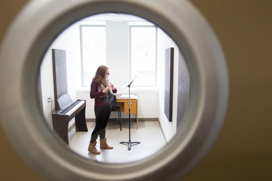 A Desautels Faculty of Music student viewed through a porthole window practicing in a practice room.