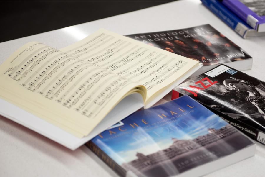 A table top with 6 music related books, one of the books is open to see a spread of pages. 