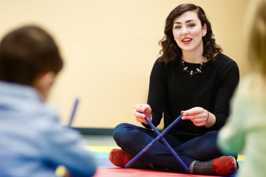 A prep studies instructor sits on the floor holding a pair of rhythm sticks.