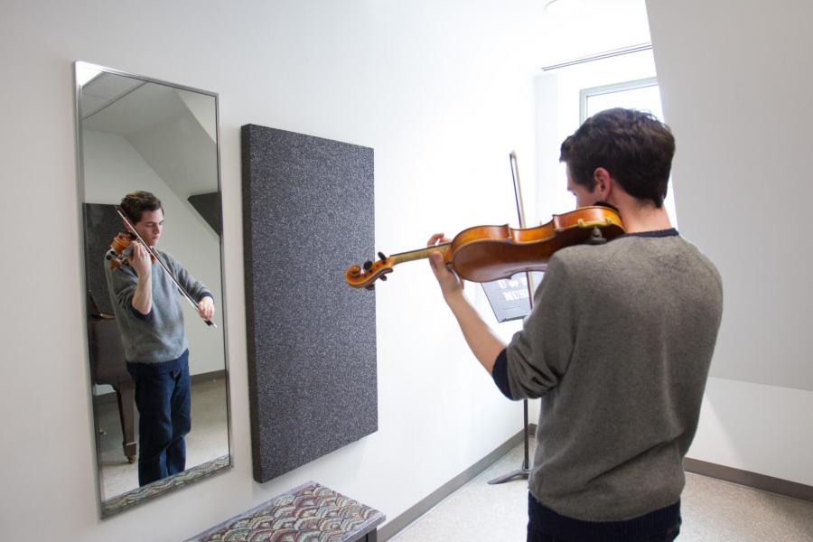 A student practices the violin in a practice room. 