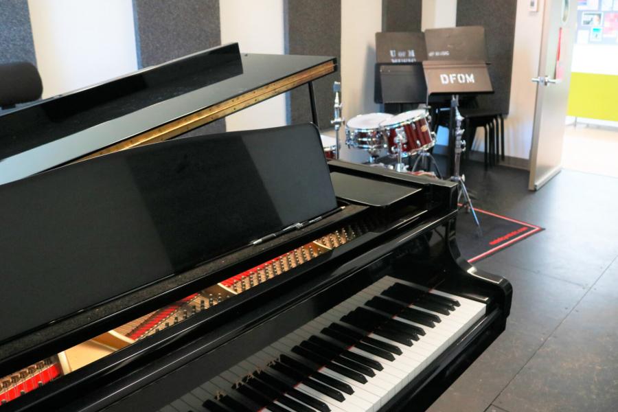An interior of a jazz ensemble practice room with a piano and full drum kit and acoustic panelling lining the walls.