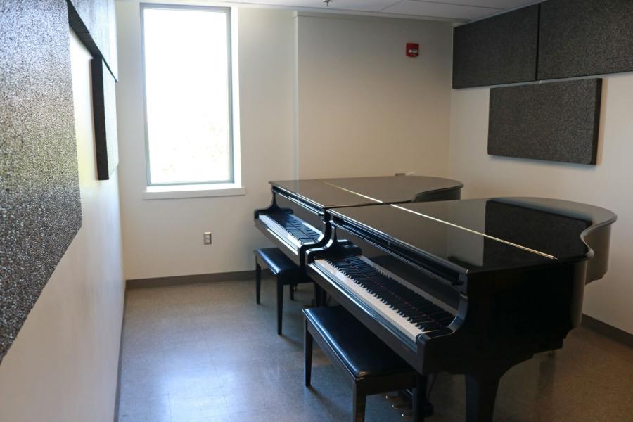 Inside a piano practice room with a tall narrow window and two pianos placed side by side.