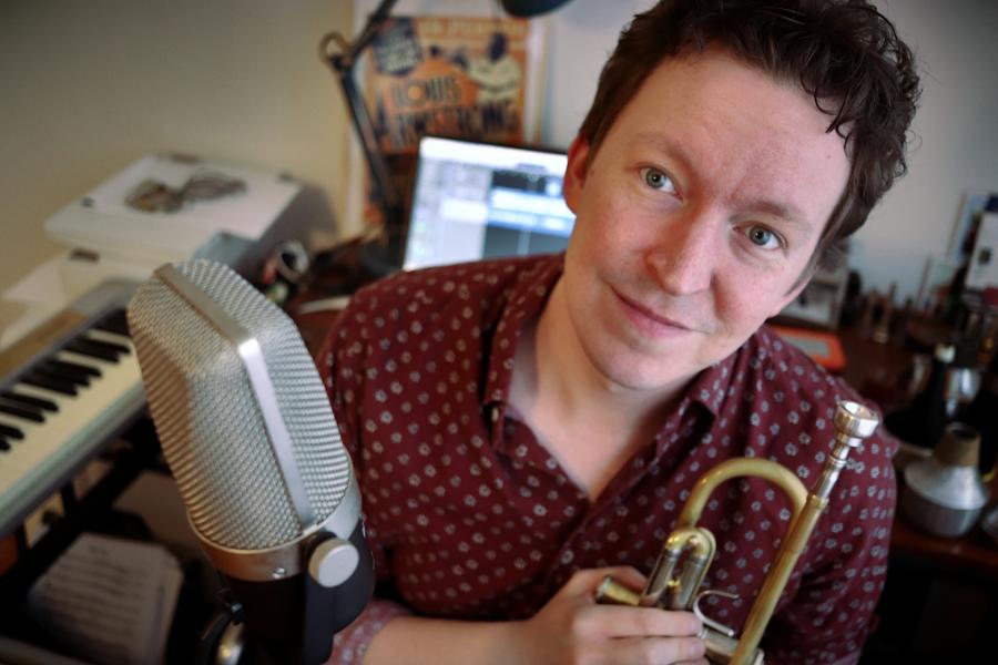 assistant professor of trumpet Jonathan Challoner sits with trumpet, microphone, and piano keyboard