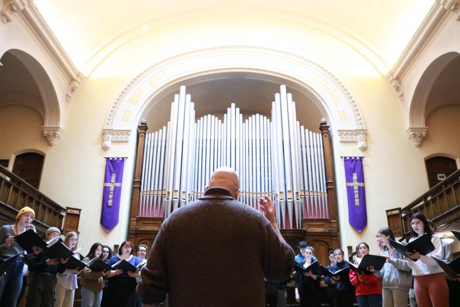 University Singers director Elroy Friesen conducting students with pipe organ in background