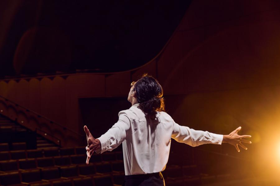 Person with their back to the camera onstage with their arms outstretched
