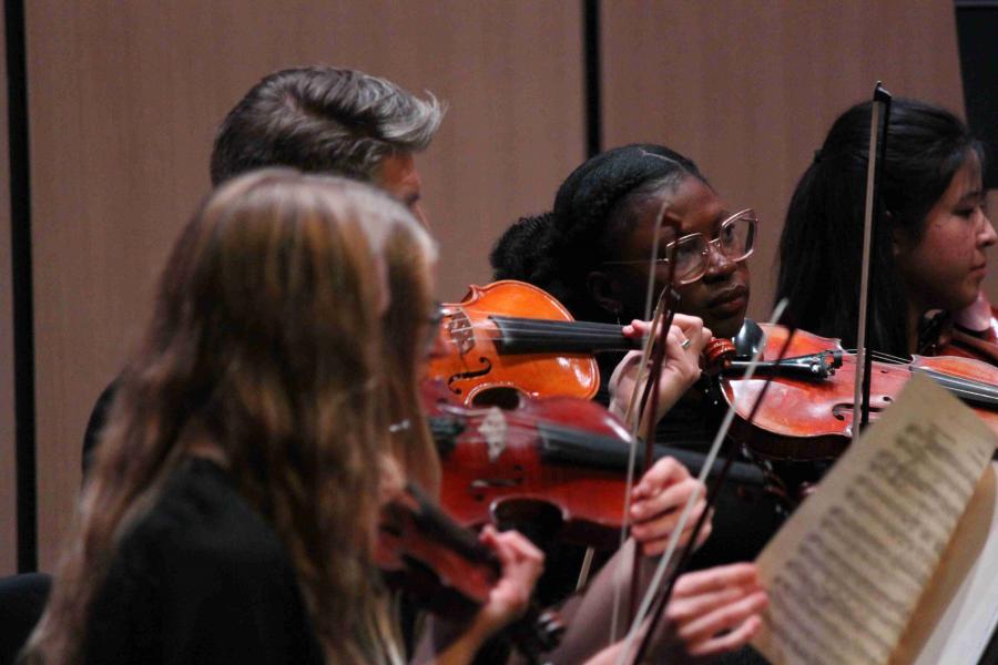 Five violinists with sheet music playing in an orchestra
