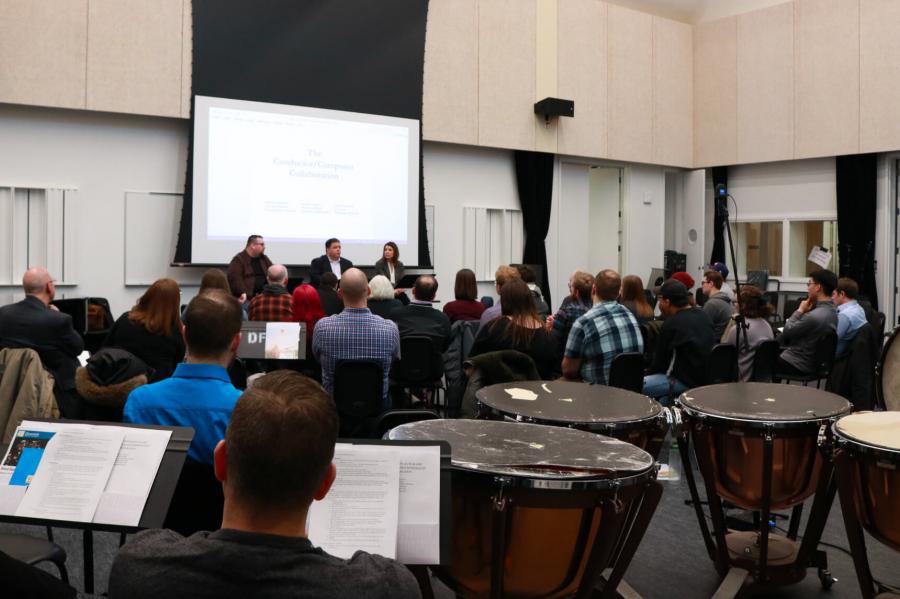 A large room with a crowd of people facing a stage with three people talking. 