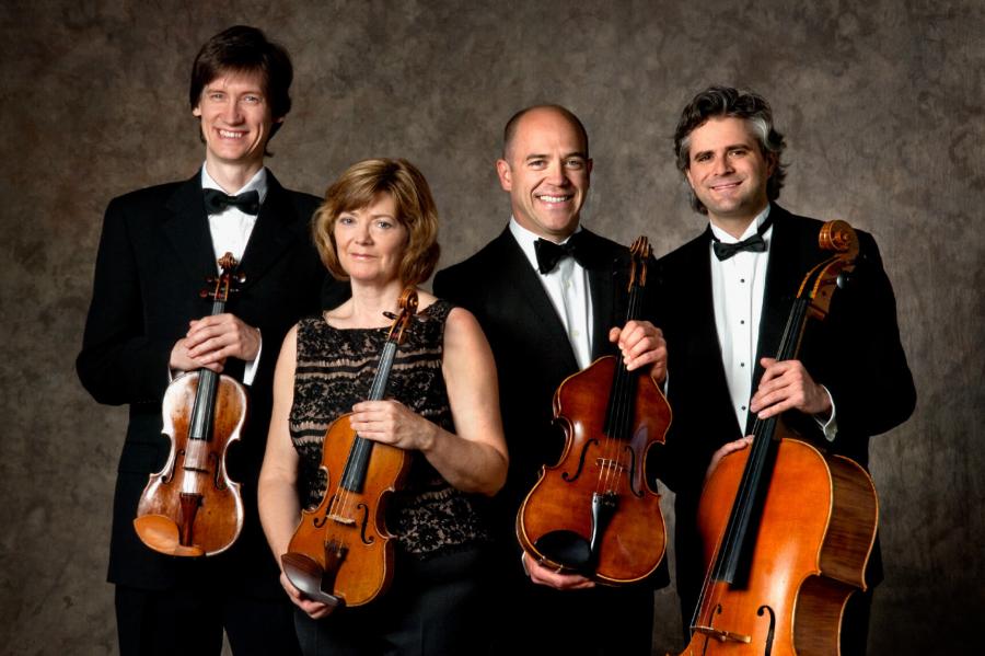 Four members of the Clearwater Quartet Gwen Hoebig, Karl Stobbe, Daniel Scholz and Yuri Hooker stand together for a photo holding their instruments.