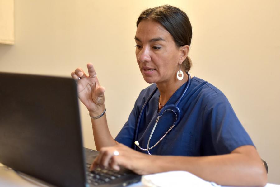 A nurse seated in front of a laptop speaking in a virtual meeting.