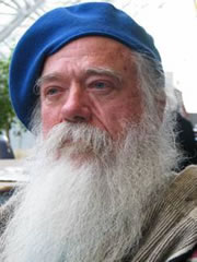 this is a picture of Jim Derksen’s face. He is sitting outside, wearing a blue beret. He has blue eyes, a long grey beard and hair.