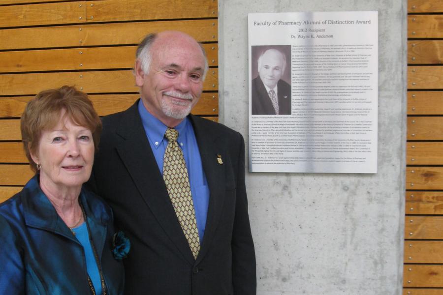 A smiling Dr. Wayne K. Anderson and his wife Lorraine stand together beside his Pharmacy Alumni of Distinction Award. 