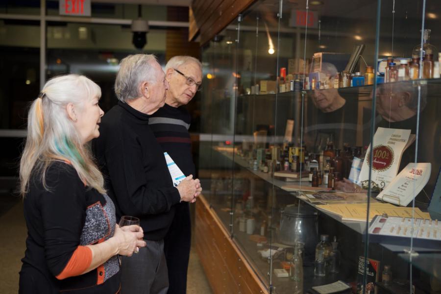Three pharmacy alumni gather around a display case to take a look at the items inside.