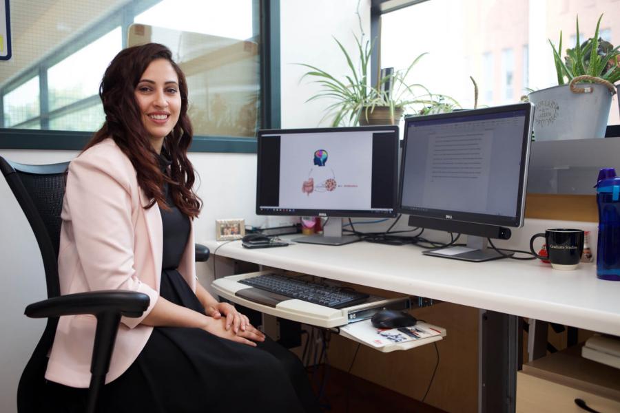 A smiling pharmacist sits at a desk in a brightly lit office working. 