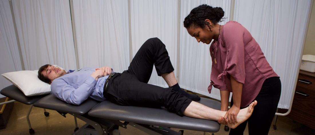 A patient lying down has their foot attended to my a physical therapist. 