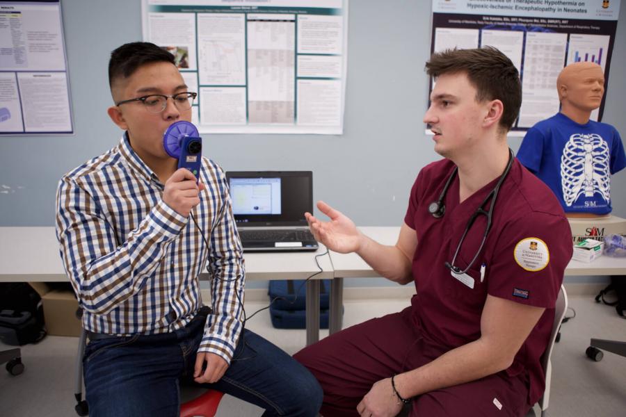 A respiratory therapy student explains to a patient how to use a medical device.