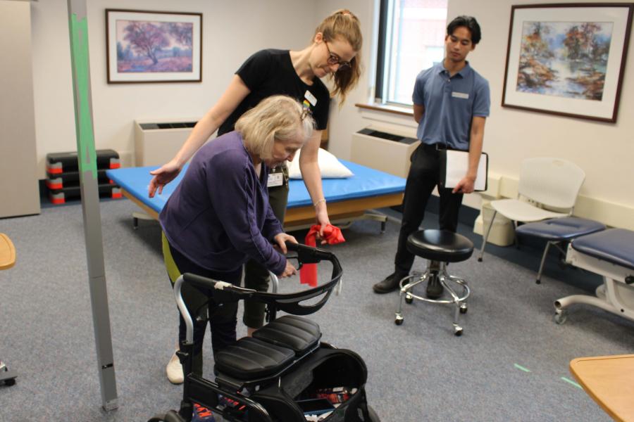 Two students assisting a senior client with a mobility device.