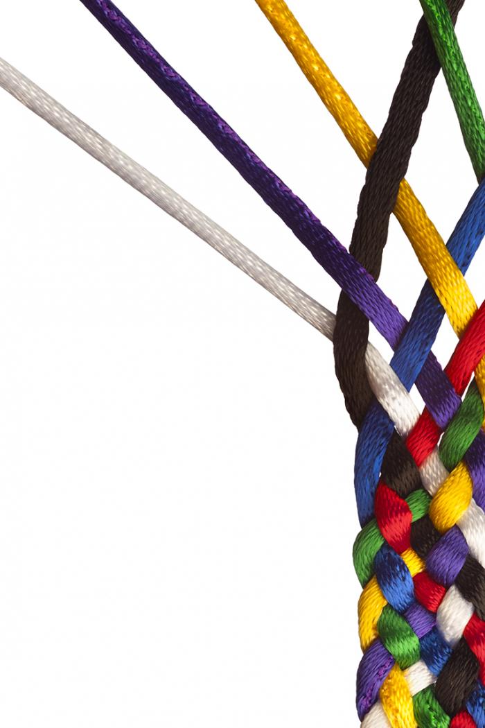 A close up of multicoloured strands of string being braided together on a white background.