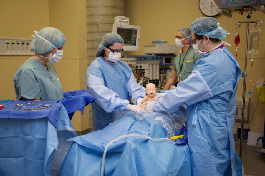 Students in scrubs at an operating table handling an infant mannequin.