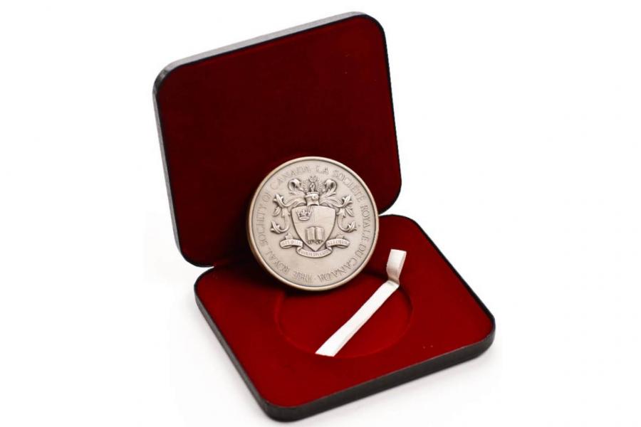 A medallion with The Royal Society of Canada insignia stamped on it, leaning inside a red velvet lined box.