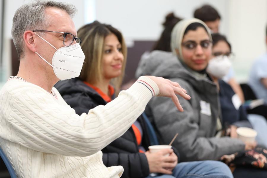 A man talking and explaining ideas with two women in the background being engaged in the conversation.