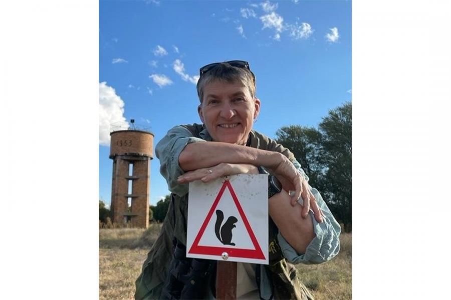 Jane Waterman smiling at the camera leaning on a road sign that warns about squirrels.