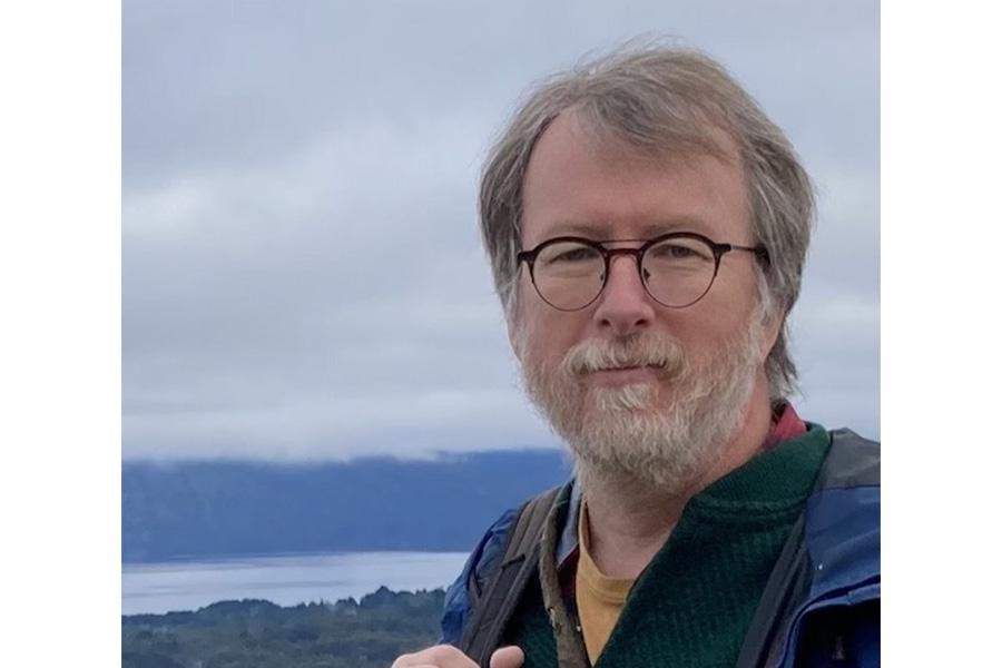 John Markham wearing an eyeglass in front of a body of water.