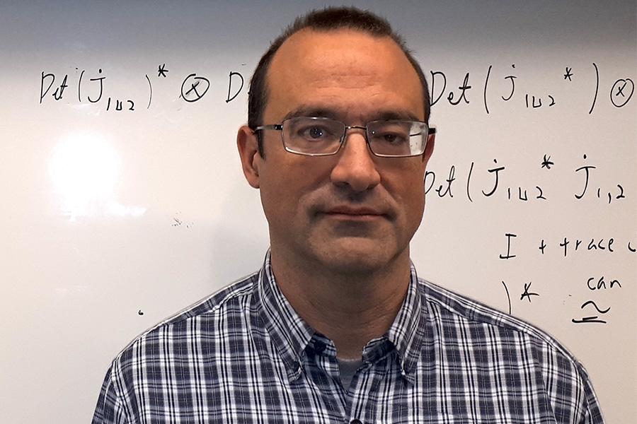 Eric Schippers wearing an eyeglass and looking at the camera in front of a white board with an equation.