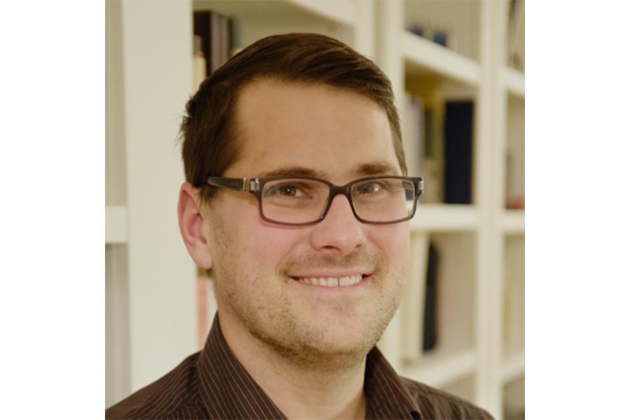 Robert Guderian wearing an eyeglass and a button down shirt smiling at the camera.