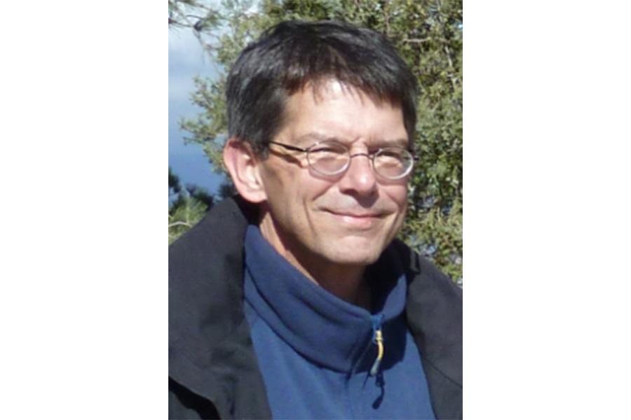 Robert Stamps wearing a blue sweater and wearing an eyeglass smiling at the camera.