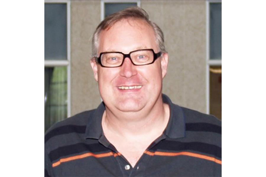 Jacky Baltes wearing a striped collar shirt and an eyeglass smiling at the camera.