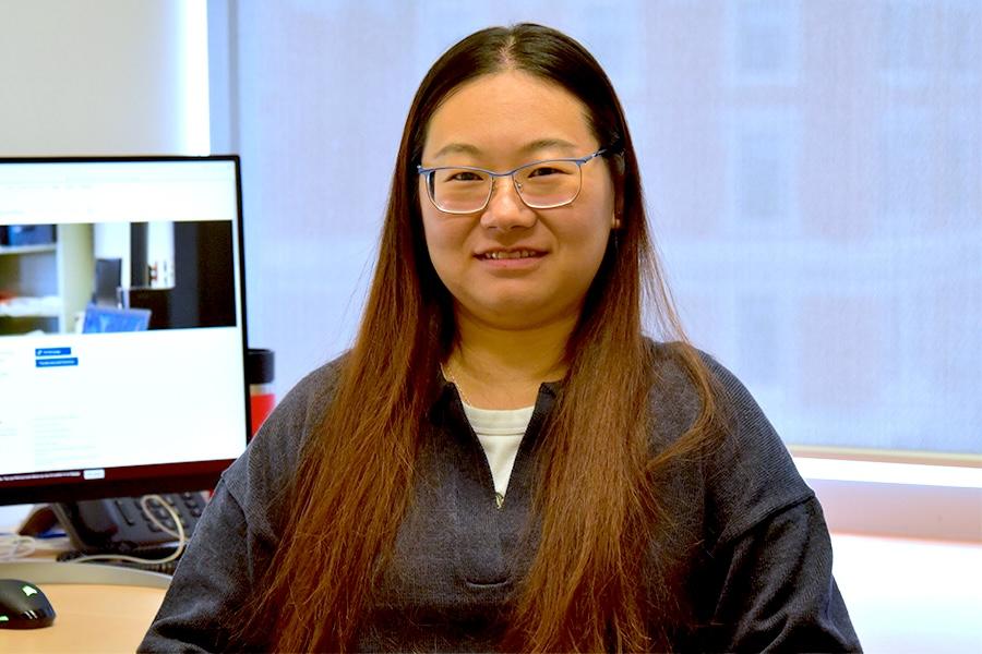 Mengjun Hu wearing a black sweater and eyeglasses smiling at the camera.