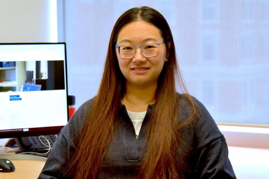 Mengjun Hu wearing a black sweater and eyeglasses smiling at the camera.