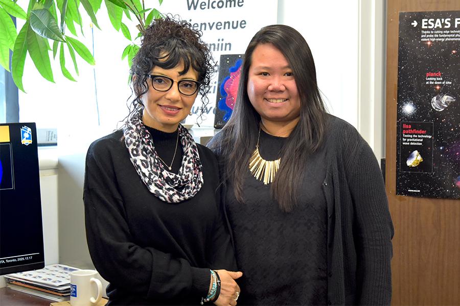 Samar Safi-Harb wearing a black top with a scarf standing beside Janette Suherli who is also wearing a black top and a gold necklace.