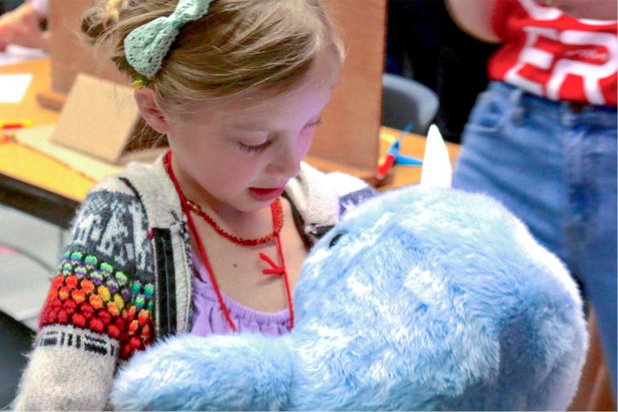 A kid hugging and looking at a robot plush.
