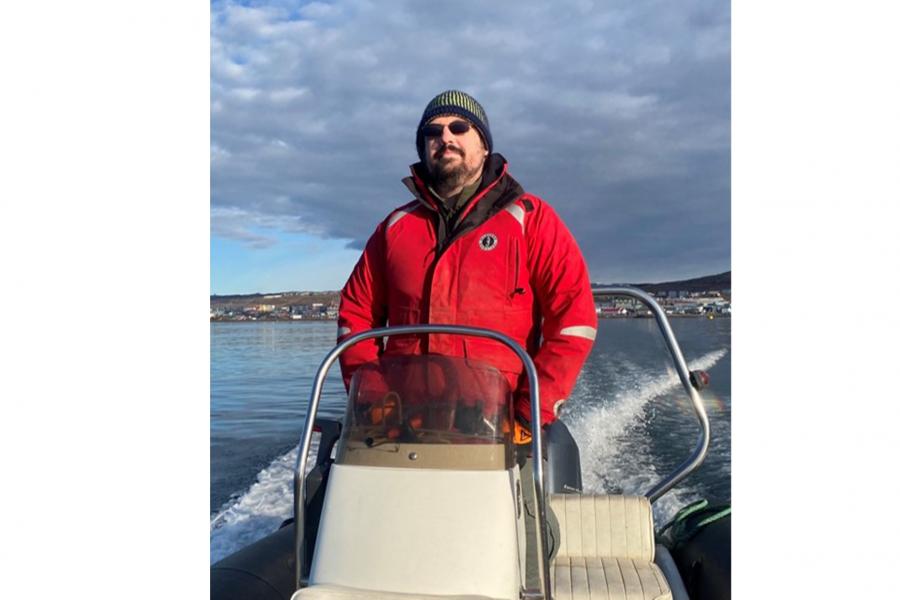 Kevin Hedges wearing a red jacket and a toque with a sunglass on a boat looking at the camera.