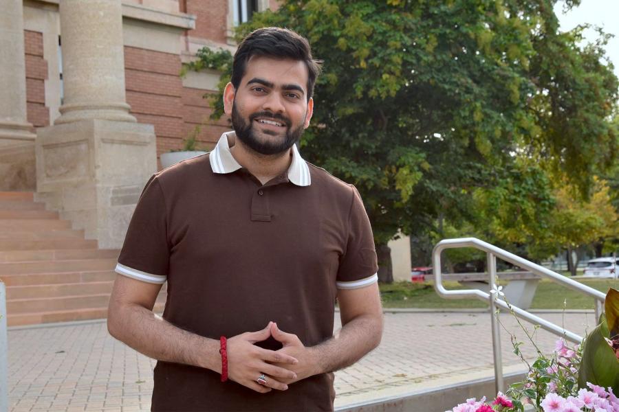Pankaj Bhagwat wearing a brown collared shirt in front of the admin building smiling at the camera.