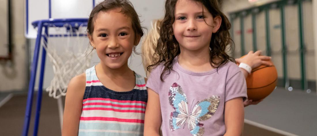 Mini U kids stand in front of a basketball net.