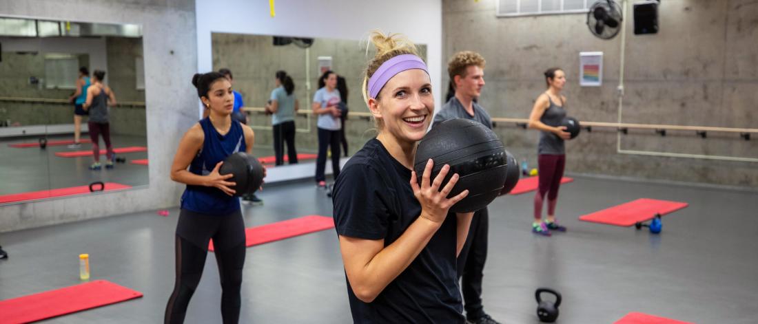 Several people in a group fitness class stand while holding medicine balls to their chests.