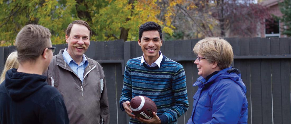 An international student stands in a backyard with his homestay host family.