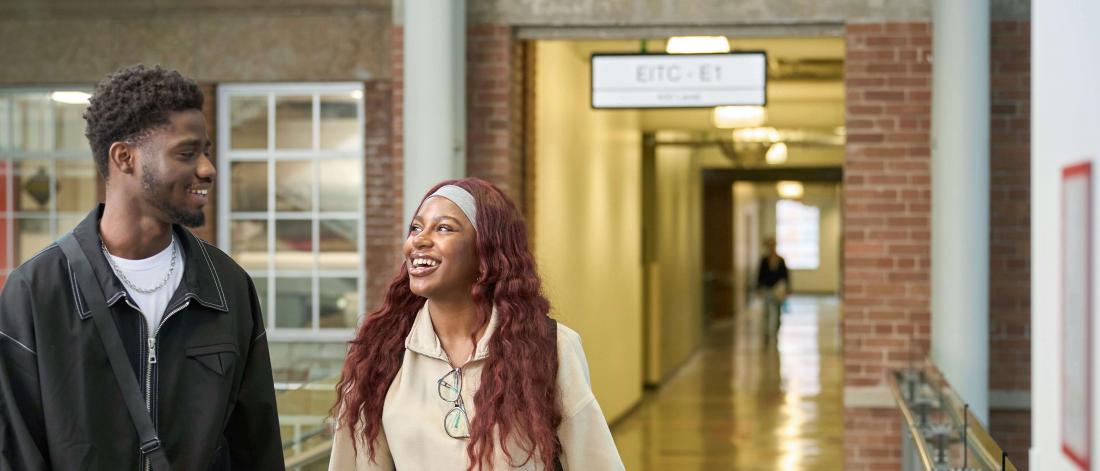 Two students walk and smile inside the Engineering building.