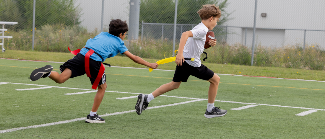 Two Mini U campers running on a field during a flag football drill