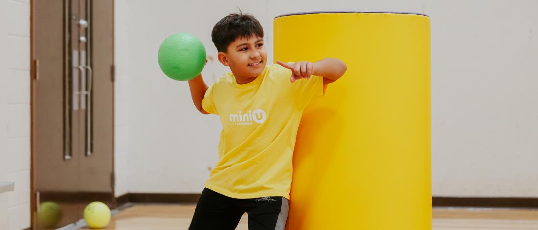 A mini u camper winding up a dodgeball throw in a gym