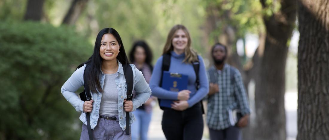 Students walking outdoors among trees on their way to class.