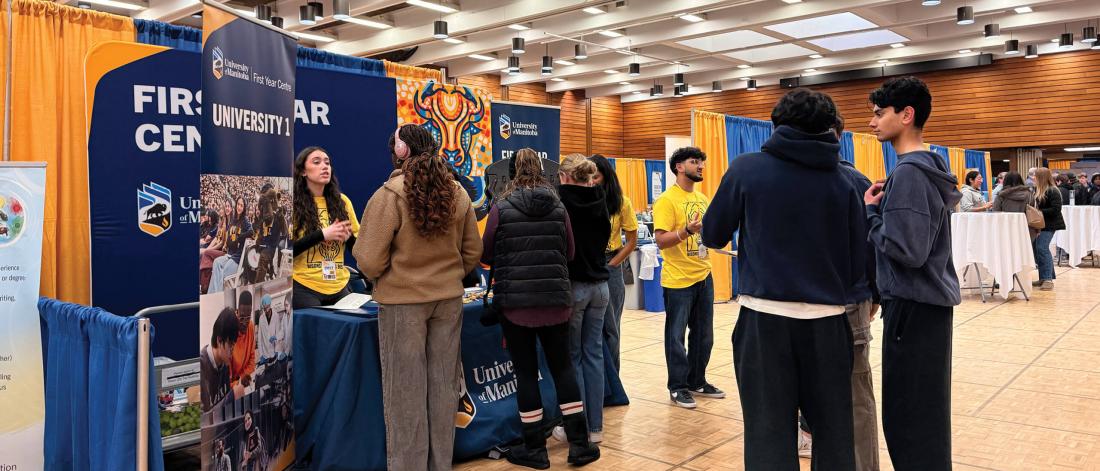 Students talk and faculty representatives talk at tables at an open house event.
