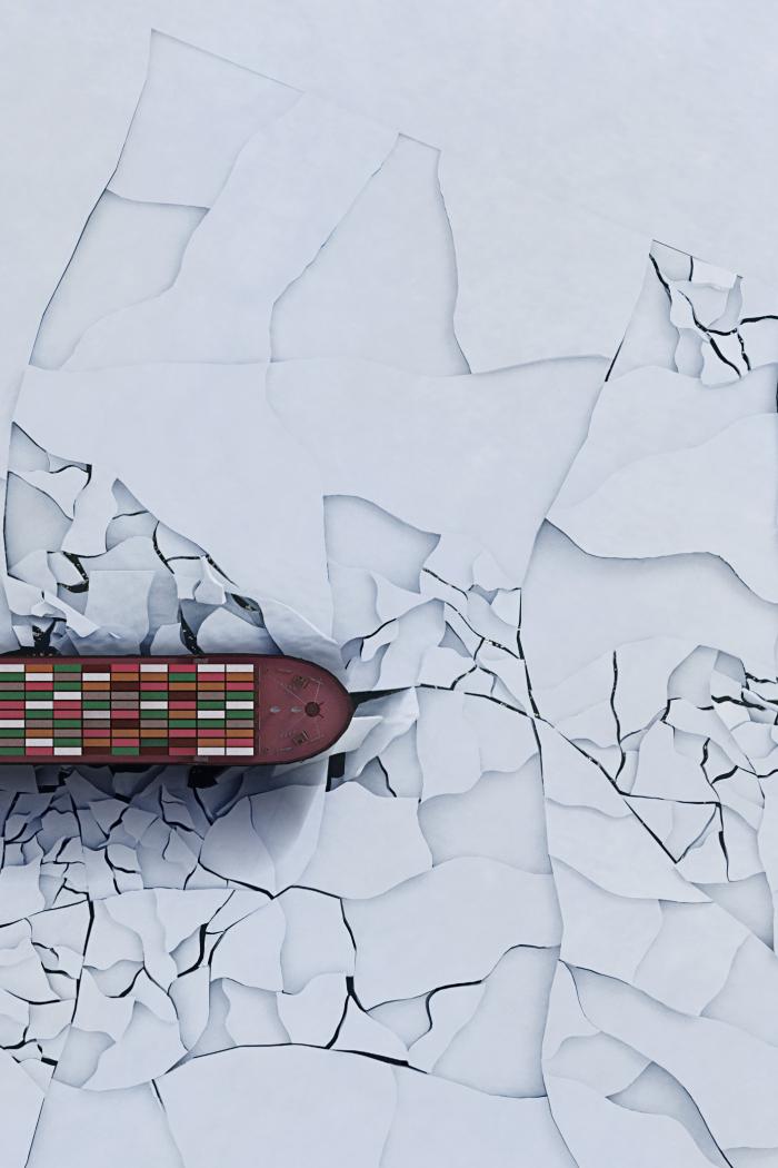 A cargo ship sails through broken ice.