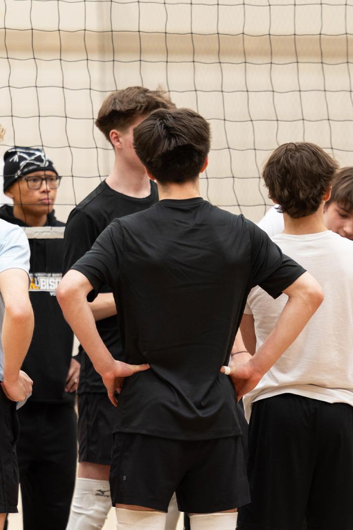 A coach talks to a group of boys in a vollyball practice huddle.