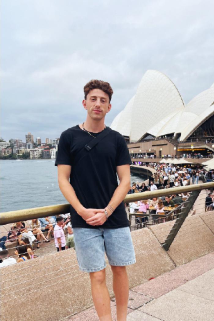 Kyle, leans against a railing while overlooking the harbour with the Sydney Opera House in the background.